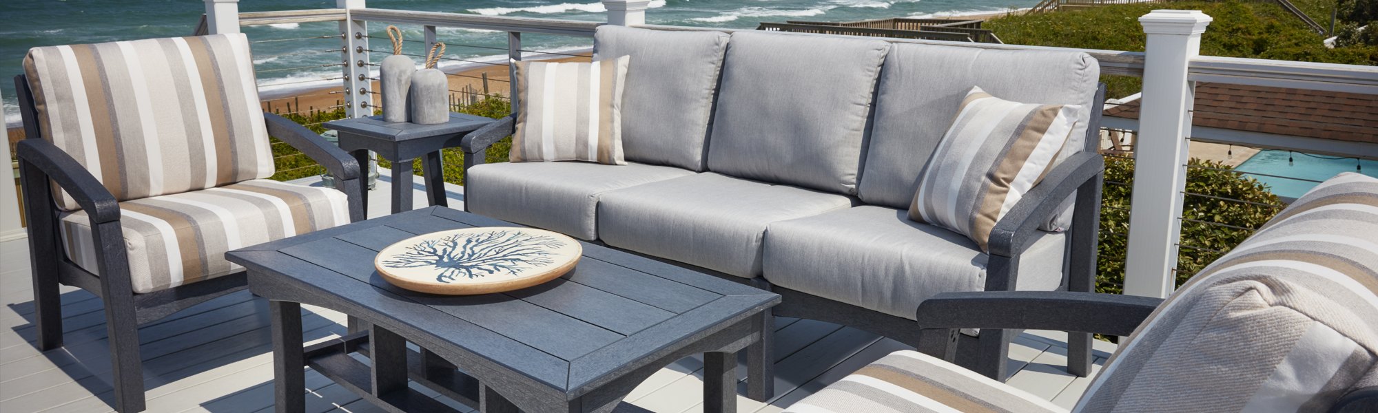 An image of a patio with grey and stripped brown patio furniture overlooking a view of the sea