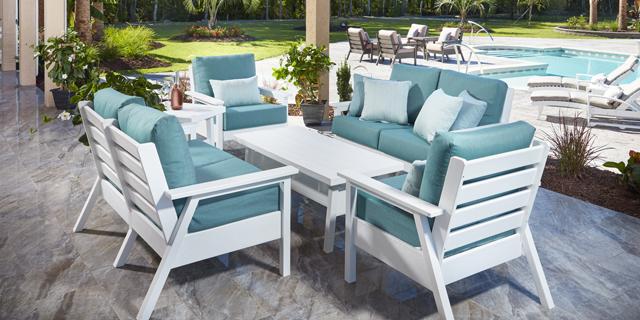 An image of an outdoor seating area with a blue cushioned patio set and a pool in the background